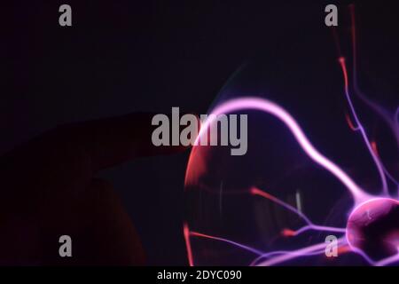 A hand touching a plasma ball with smooth magenta Stock Photo