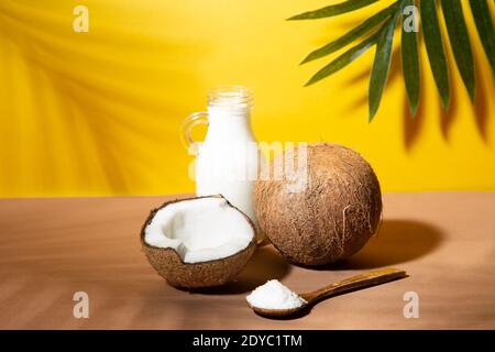 Coconuts, coconut milk and shredded coconut on yellow and brown background with palm shades. Stock Photo