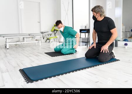 Physiotherapist assisting man in performing exercise on mat. High quality photo Stock Photo