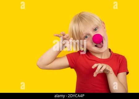 Gay boy in red shirt and with clown nose making grimaces. Portrait on yellow background. Stock Photo