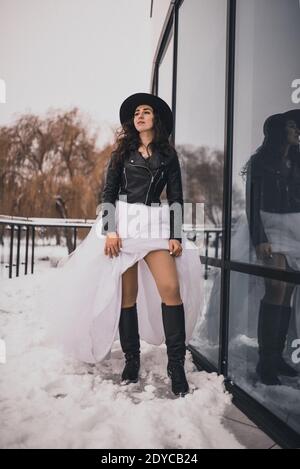 brunette bride woman in wedding white dress, black leather biker jacket and  black hat in high boots in winter on the snow. stylish fashion clothing el  Stock Photo - Alamy
