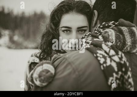 young man and woman stand kissing and hugging. bride and groom in love couple in knitted scarf and mittens in winter with snow and snowflakes. wedding Stock Photo
