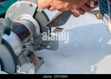 Close-up of men's hands sharpening an axe on an electric sharpener. Repair of home tools with Your own hands. Stock Photo