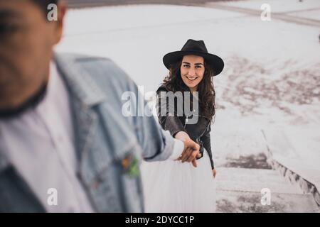 Mexican Hispanic man in oversized denim jacket and woman in hat leather biker jacket kissing hugging laughing walking.groom bride wedding love couple Stock Photo