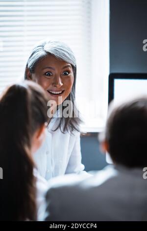 Mature Asian supervisor woman cheerfully talking to employees sitting one against another. Asian mature business woman talking to a managers sitting Stock Photo