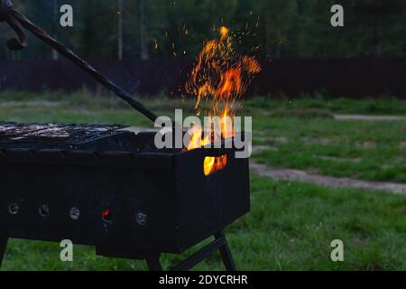 Meat is grilled. A man stirring coals with a hot poker. Sparks fly from fire in grill. Outdoor cooking. Picnic, weekend Stock Photo