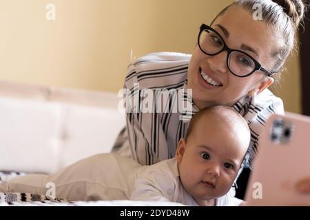 Childhood, motherhood, family concepts - successful smiling rich business woman Lady mother sit on bed with infant child baby talking on phone by Stock Photo