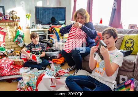 A family excitedly open Christmas presents together at home on Christmas day. Stock Photo