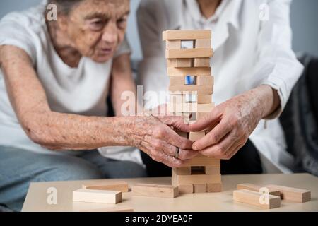 Senior woman playing Jenga, build tower of blocks. Elderly doctor in white lab coat, supporting senior patient, developing logic, fine motor skills Stock Photo