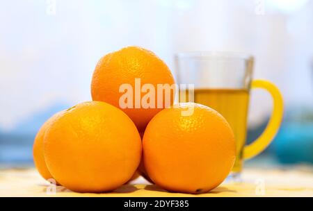 A cup of orange tea and fresh, ripe, juicy oranges on the table Stock Photo