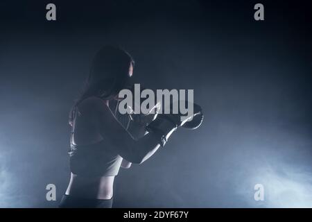 Side view of a silhouette young woman with boxing gloves making a direct hit. Stock Photo