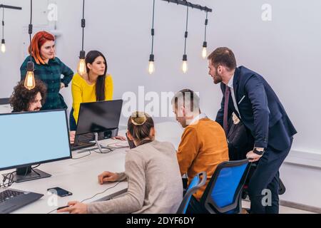 Handsome young executive explaining new employees an online task on theirs computers Stock Photo