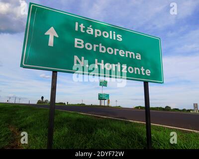 Metal plate giving the direction of three cities (names displayed in portuguese) with a big white arrow placed at the sideway of a countryside route Stock Photo