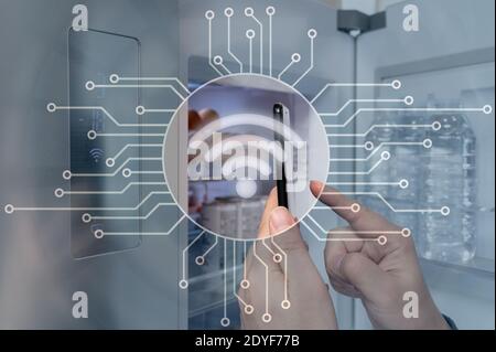 The hand of the man who controls the refrigerator with his smartphone. Internet of Things Concept Stock Photo