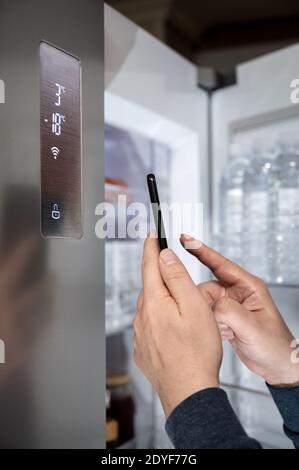 The hand of the man who controls the refrigerator with his smartphone. Internet of Things Concept Stock Photo