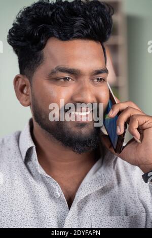 Close up of Smiling young Indian man busy talking or having conversation on mobile phone. Stock Photo