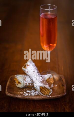 Pumpkiln cannolli covered in powedered sugar on a wooden platter with a glass of rose champagne Stock Photo