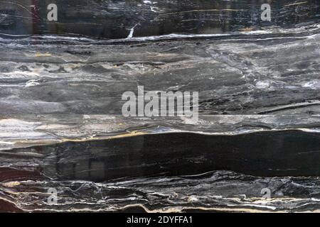 Glossy marble with black and gray veins. A sample of black marble with a pronounced texture. Stock Photo