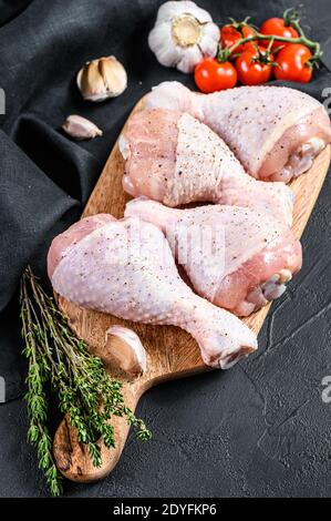 Raw fresh chicken drumsticks with spices and vegetables on a wooden cutting board. Black background. Top view Stock Photo