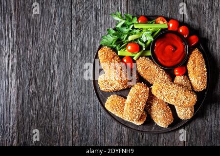 Deep-fried italian suppli al telefono rice croquettes stuffed with mozzarella served on a black plate with celery stalks, tomatoes, and ketchup on a d Stock Photo