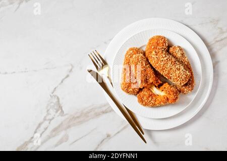 Italian suppli al telefono or rice croquettes stuffed with mozzarella served on a white plate with golden cutlery on a light marble background, top vi Stock Photo