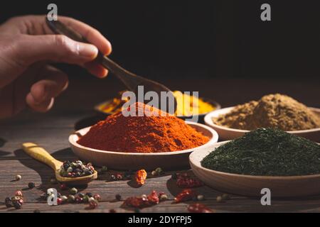 Various colorful herbs and spices on wooden table. hand with a spoon . Dark background, selective focus. with copy space. Cooking ingredients and cond Stock Photo