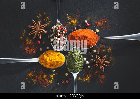 Star anis and spoons with pepper, paprika, parsley and turmeric on black background with copy space, top view. Cooking ingredients and condiments conc Stock Photo