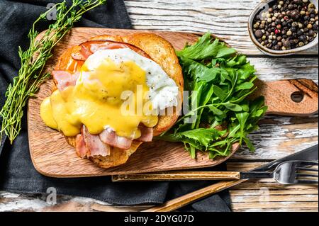 Breakfast Burger with bacon, egg Benedict, hollandaise sauce on brioche bun. Garnish with arugula salad. White background. Top view Stock Photo