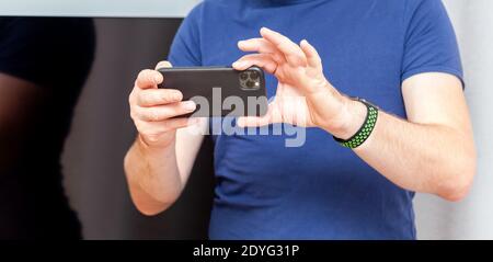 Anonymous young adult, man holding Iphone 11 in hands taking photos, closeup, Apple Watch on wrist. Apple products consumer lifestyle, smartphone Stock Photo