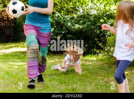 Child falling down running, playing ball with family in the garden, injury concept. Kids outdoors sport activity accident, fall on the grass Stock Photo