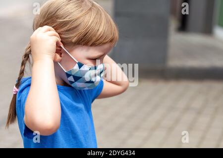 Lone little child, school age girl putting on or taking off her anti viral face mask, portrait, closeup, copy space Covid 19, corona virus pandemic Stock Photo