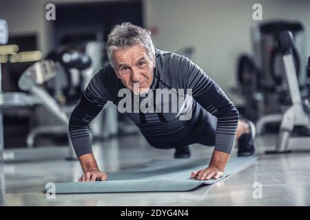 Age is just a number to a man with grey hair doing pushups in a gym. Stock Photo