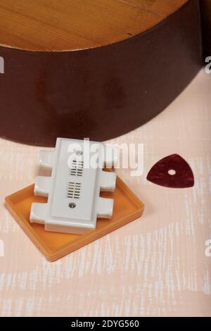 Fragment of acoustic guitar, tuning fork and pick. Against a background painted in white and beige. Stock Photo