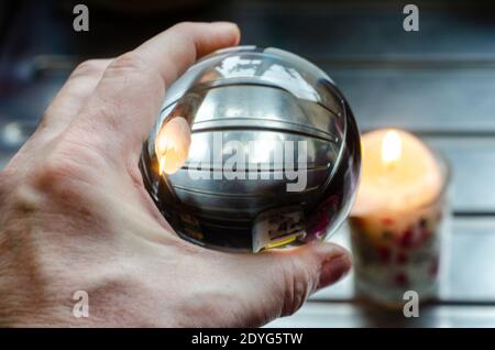 A candle on a draining board is seen upside down in a glass crystal ball due to the effect of refraction as the glass ball acts as a lens. Stock Photo