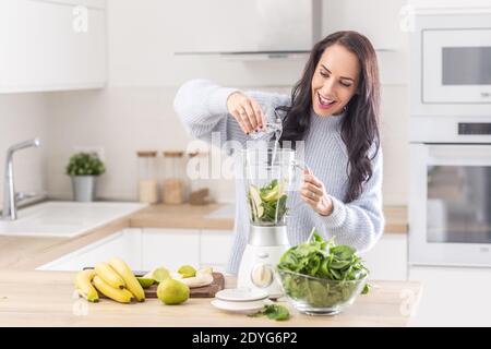 Woman adds water into a mixer for a spinach, banana, and apple smoothie. Stock Photo