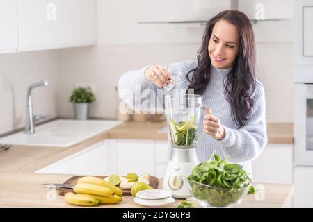 Woman adds water into a mixer for a spinach, banana, and apple smoothie. Stock Photo