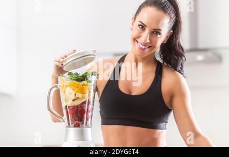 Colorful nutrition of spinach, oranges, bananas and strawberries put into a blender by a fit woman. Stock Photo