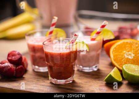 Different colors of red and pink smoothies in cups with paper straws on a kitchen table. Stock Photo