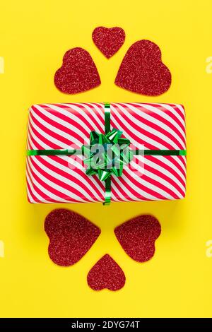 Valentine's Day card. Wrapped gift. Minimalistic design. Festive present and red hearts on a yellow paper background, romantic symbolic celebration of Stock Photo