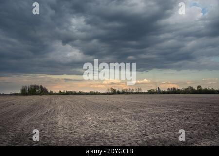 Plowed field, dark rainy clouds on the sky, spring rural view Stock Photo