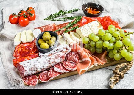 Italian antipasto, wooden cutting board with prosciutto, ham, parma, goat and Camembert cheese, olives, grapes. antipasti. Gray background. Top view Stock Photo