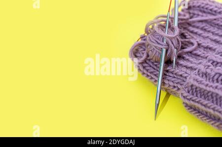 The cap is connected by circular spokes on the wire on a yellow background. Process of knitting. Best hobby. Stock Photo