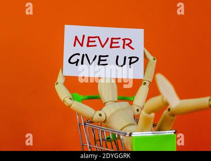 Never give up symbol. White sheet of paper. Words 'never give up'. Wooden model of a human in a shopping cart. Beautiful orange background. Business a Stock Photo