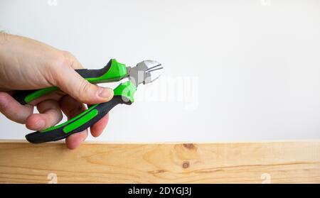A male hand holds a wire cutters on a wooden bar. Beautiful white background. Copy space. Building concept. Stock Photo