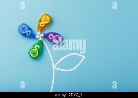 Stationery correction tapes in the shape of a flower of different colors on a blue background. Free space. The view from the top. Blue, green, yellow, Stock Photo