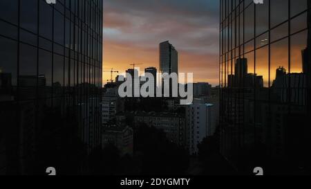 Warsaw skyline at night. Drone passing between two skyscrapers revealing red sky and silhouettes of the building in the distance. High quality photo Stock Photo