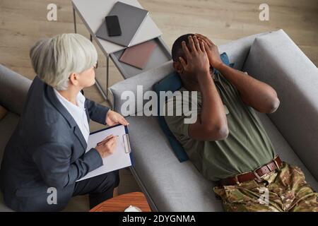 Psychologist making notes during therapy session with sad male soldier Stock Photo