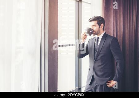 Thoughtful businessman drinking coffee, looking through window at big modern city, having break, deep in thoughts, enjoying view, waiting for meeting Stock Photo