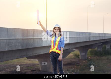 Beautiful Asian female engineer in white safety hard hat doing job at construction site outside office. Idea for modern working woman hightway road Stock Photo