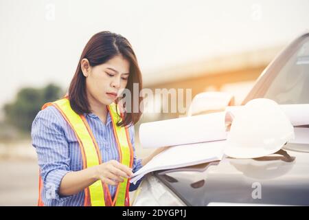 Beautiful Asian female engineer in white safety hard hat doing job at construction site outside office. Idea for modern working woman hightway road Stock Photo